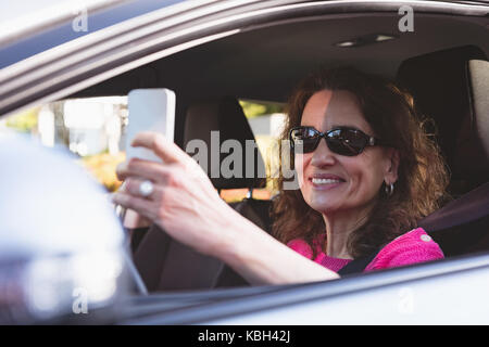 Happy woman using mobile phone while driving car Stock Photo