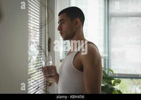 Thoughtful man looking through window blinds at home Stock Photo