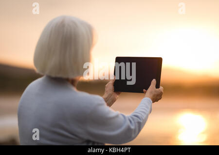 Senior woman using digital tablet at beach during sunset Stock Photo
