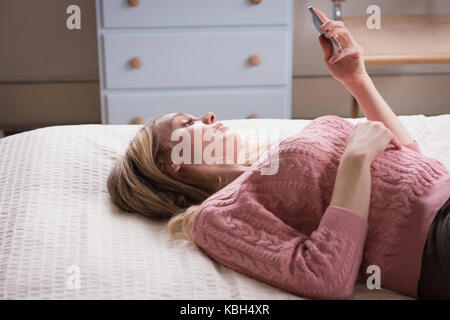 Relaxed young woman using phone while lying down on bed at home Stock Photo