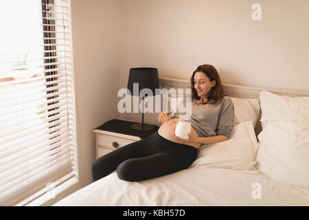 Pregnant woman applying cream on stomach on bed Stock Photo