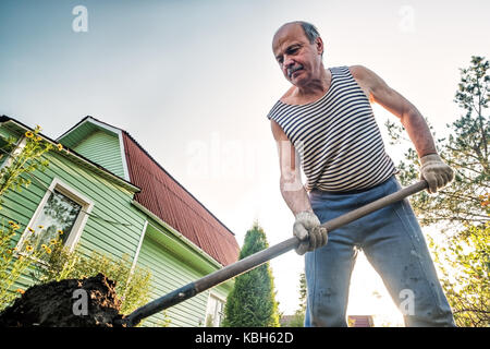 Portrait of caucasian male farmer with shovel digging the land in the country house Stock Photo