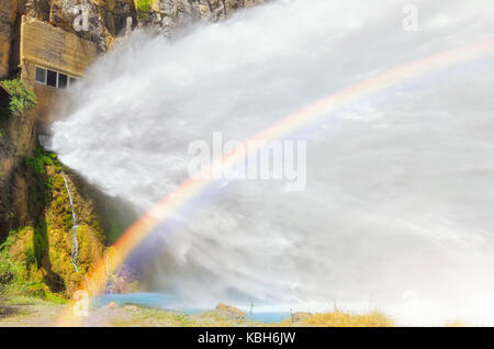 Artificial big waterfall formed by the spillway of hydroelectric dam. Water flowing, strongly, towards river. Beautiful colorful and energy scene.