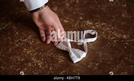 Groom's hand takes a bow tie. Preparing to wedding day. The man takes the bow-tie. Wedding accessories. Groom holding brown bow tie in his hand. Man holding bow tie. Elegant gentleman clother. Wedding Stock Photo