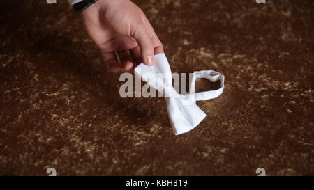 Groom's hand takes a bow tie. Preparing to wedding day. The man takes the bow-tie. Wedding accessories. Groom holding brown bow tie in his hand. Man holding bow tie. Elegant gentleman clother. Wedding Stock Photo