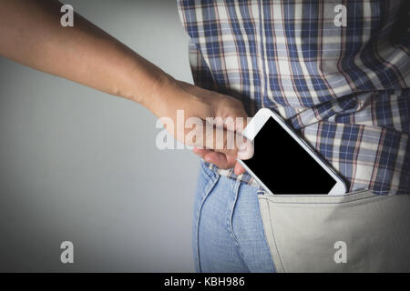 Close-up of a the hand of thief stealing the smart phone to a woman. Thief stealing mobile phone from back pocket of a woman. Stock Photo