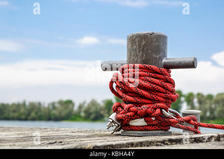 Worn old rusty mooring bollard with heavy ropes on the deck of a ship, closeup. Stock Photo