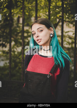 Street punk or hipster girl enjoying empty old European street. Portrait of teen girl with blue dyed hair,piercing in nose,violet lenses and unusual h Stock Photo