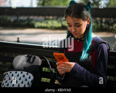 hipster girl playing tetris game in European park. Portrait of teen girl with blue dyed hair,piercing in nose,violet lenses and unusual hairstyle.Old  Stock Photo