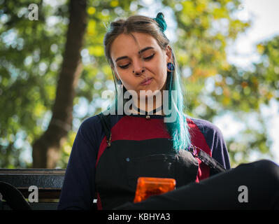 hipster girl playing tetris game in European park. Portrait of teen girl with blue dyed hair,piercing in nose,violet lenses and unusual hairstyle.Old  Stock Photo
