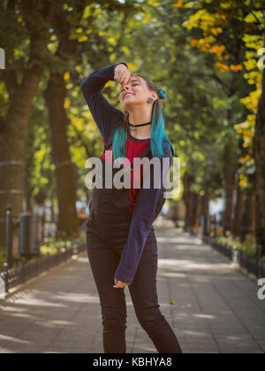 Street punk or hipster girl enjoying empty old European park. Portrait of teen girl with blue dyed hair,piercing in nose,violet lenses and unusual hai Stock Photo