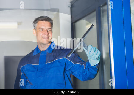 Happy mature male worker cleaning glass with squeegee Stock Photo
