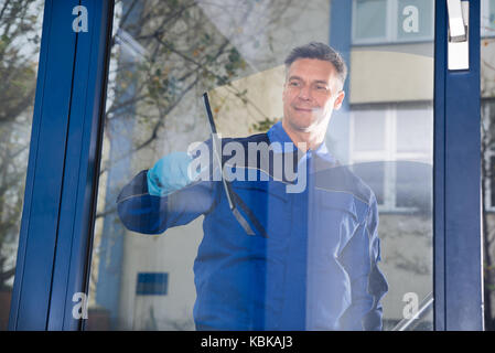 Happy mature male worker cleaning glass with squeegee Stock Photo