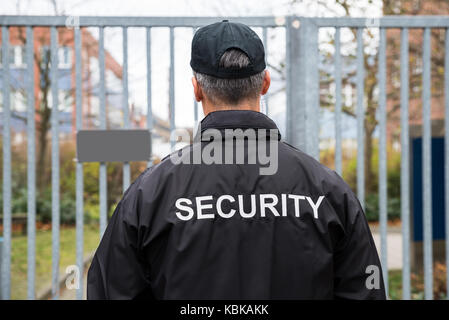 Rear view of mature security guard standing in front of gate Stock Photo