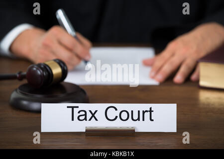 Tax court nameplate on table with judge writing on paper in background at courthouse Stock Photo