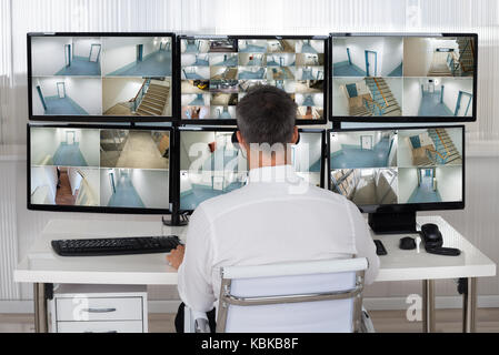 Rear view of security system operator looking at CCTV footage at desk in office Stock Photo