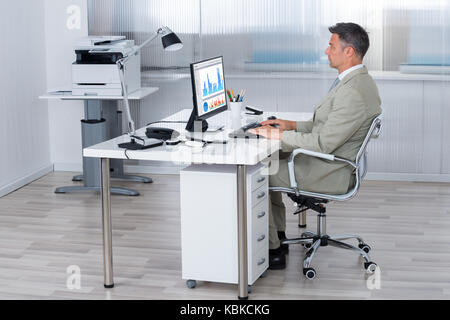 Full length side view of businessman using computer at desk in office Stock Photo