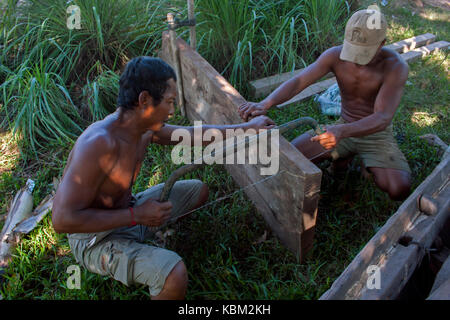 Two poor Cambodian fisherman are sawing wood as they repair a wooden fishing boat in Kampong Cham Province, Cambodia. Stock Photo