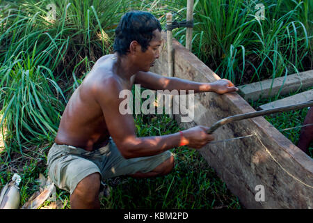 A poor Cambodian fisherman is sawing wood as he repairs a wooden fishing boat in Kampong Cham Province, Cambodia. Stock Photo