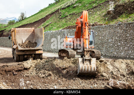 Excavator loading dirt into a truck at road construstion site Stock Photo