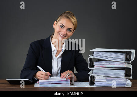 Portrait of smiling businesswoman writing on document at desk over gray background Stock Photo