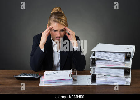 Stressed businesswoman massaging head while looking at folders over gray background Stock Photo