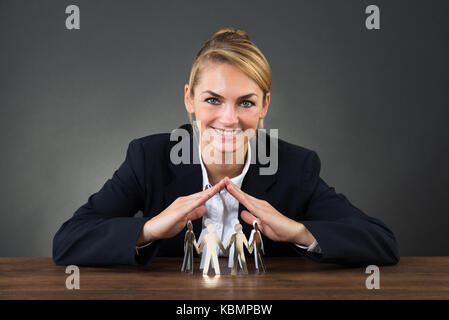 Smiling young businesswoman with hands over paper team on desk over gray background Stock Photo