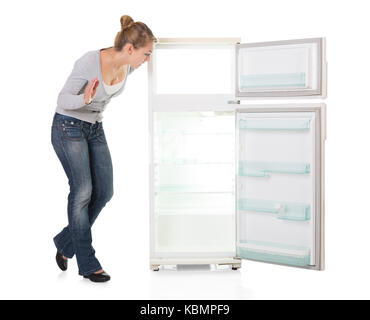 Full length of young woman looking at empty refrigerator over white background Stock Photo