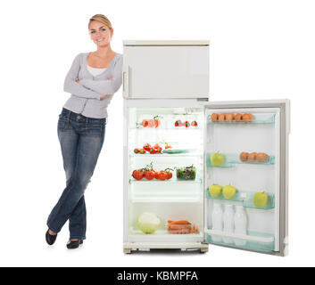 Portrait of confident young woman leaning on open refrigerator over white background Stock Photo