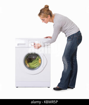 Full length side view of young woman using washing machine over white background Stock Photo