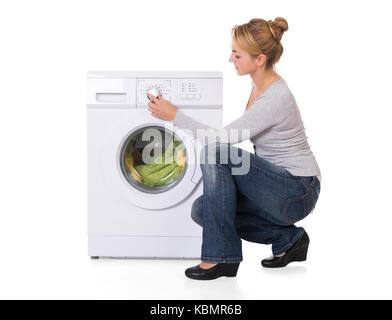 Full length side view of young woman crouching while using washing machine over white background Stock Photo