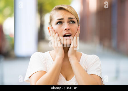 Shocked young woman with hands on face looking up Stock Photo