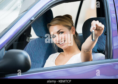 Portrait of happy young woman showing key in new car Stock Photo
