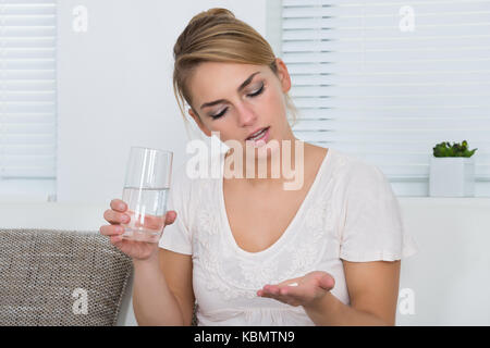 Young woman holding tablets and water glass while sitting on sofa at home Stock Photo