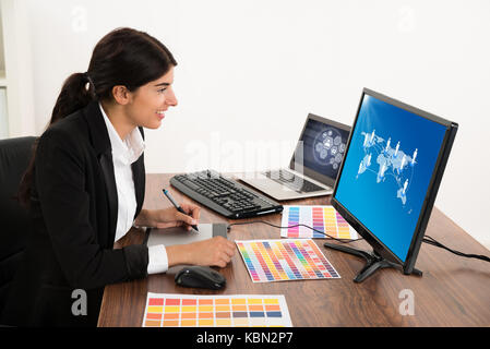 Happy Female Designer Looking At Computer While Using Graphic Tablet At Desk. Photographer owns copyright for images on screen Stock Photo