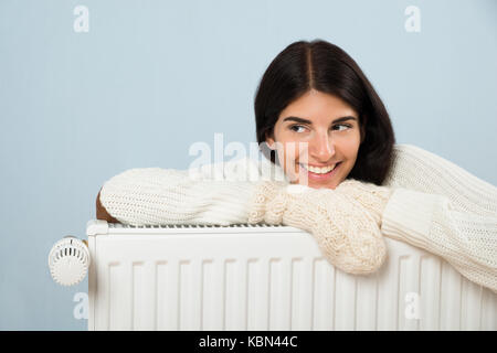 Young Happy Woman In Sweater Leaning On Radiator Stock Photo