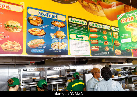 Worker's behind the counter at Nathan's Famous hot dog restaurant with the large menu board. Stock Photo