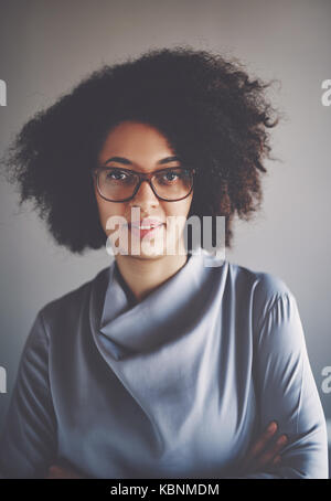 Portrait of a focused young African businesswoman wearing glasses and standing alone in an office with her arms crossed Stock Photo