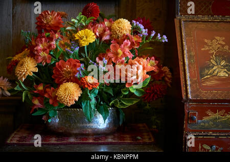 A rustic country flower arrangement beside a red and orange antique chinese cabinet Stock Photo