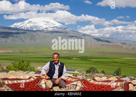 Kurdish man sitting on carpet, with the Mt Ararat in the background, in Dogubeyazit, Turkey. Stock Photo