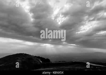 View of a valley from a mountain, with sun rays coming out through the clouds Stock Photo