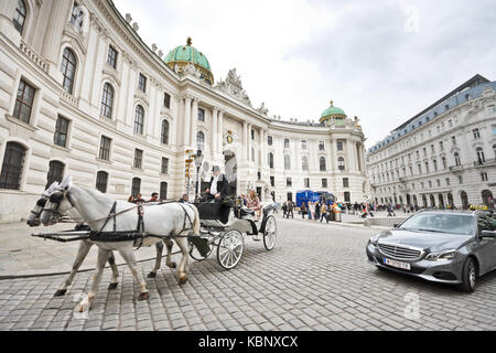 Two kinds of taxi: Horse-drawn carriage called fiaker passes by the Hofburg palace at Michaelerplatz and crosses paths with engine-driven taxi. Stock Photo