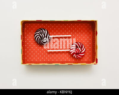 Lollipops Flat lay with white background Two colored Lollipops are lying in red gift box with polka dot pattern Classic round red-white and brown-whit Stock Photo