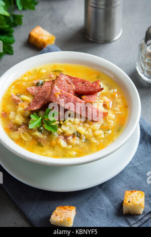 Split pea soup with smoked ham and croutons on grey background. Healthy homemade thick split soup for winter lunch. Stock Photo