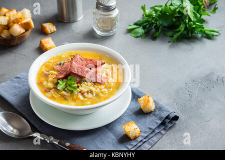 Split pea soup with smoked ham and croutons on grey background. Healthy homemade thick split soup for winter lunch. Stock Photo