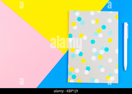 Top view of paper notebook with pen on blue, yellow and pink background. Stock Photo