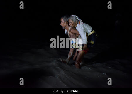 COX’S BAZAR, BANGLADESH – SEPTEMBER 30, 2017: On a dark night Myanmar’s minority Rohingya Muslim refugees disembark from a boat on the bank of Naf Riv Stock Photo