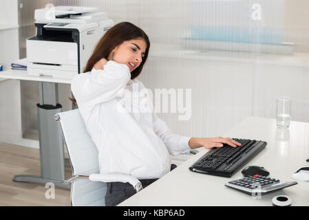 Young pregnant businesswoman suffering from neck pain while using computer in office Stock Photo