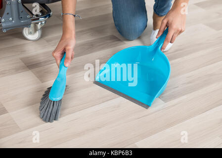 Cropped image of female cleaner sweeping wooden floor with small broom and dustpan in office Stock Photo