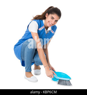 Full length of young female cleaner sweeping with small broom and dustpan on white background Stock Photo